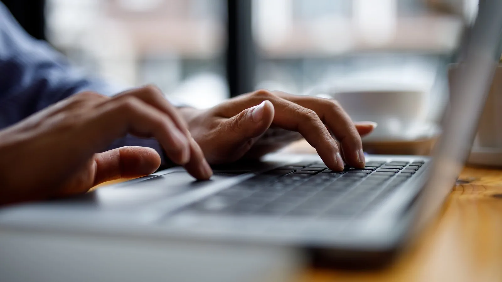 Close-up of hands typing on a laptop keyboard at a desk