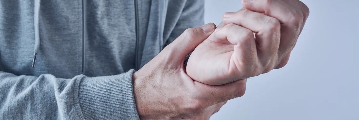 A man in a grey hooded top holding his own wrist with the opposite hand.