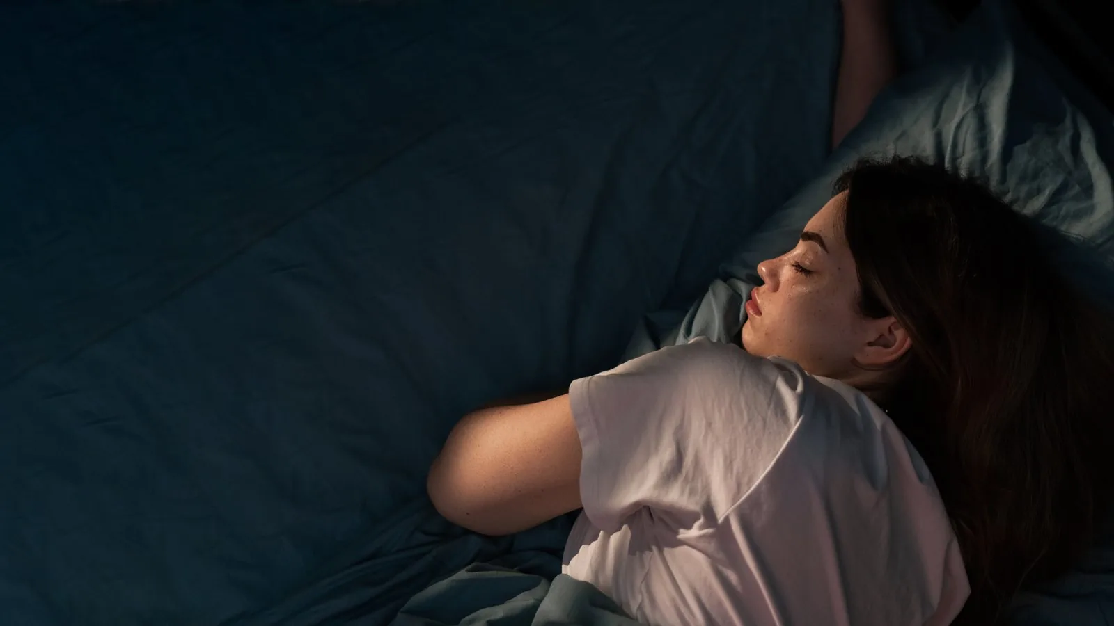 A woman asleep on her side at night with one arm curled up near her face