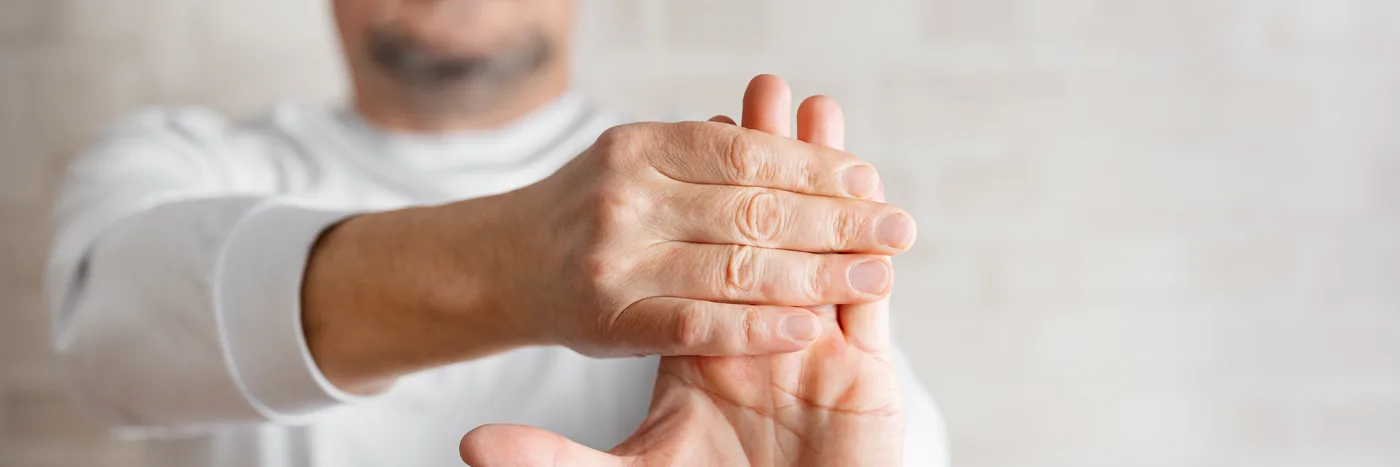 A man in a white top bending the fingers of one hand back with the other in a wrist stretch.